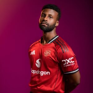 Focused portrait of a soccer player wearing a Manchester jersey with a bold purple backdrop.